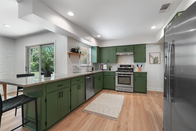 kitchen featuring green cabinetry, under cabinet range hood, open shelves, a peninsula, and appliances with stainless steel finishes