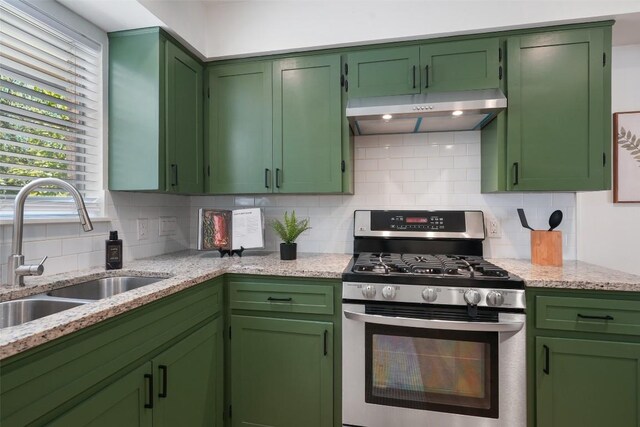 kitchen with light stone counters, under cabinet range hood, backsplash, a sink, and stainless steel range with gas cooktop
