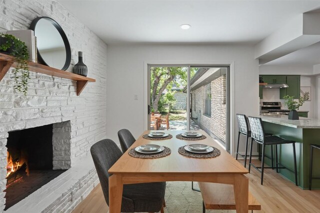 dining room featuring light wood-type flooring and a stone fireplace