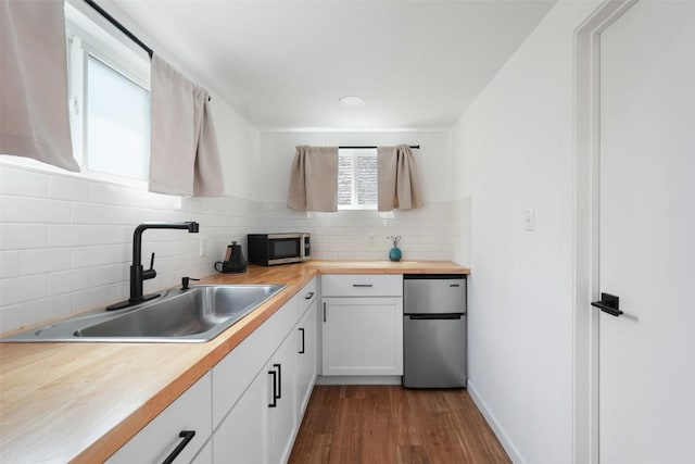 kitchen with dark wood-style floors, a sink, stainless steel microwave, backsplash, and refrigerator