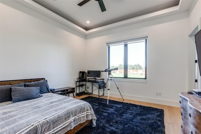 bedroom with a tray ceiling, wood finished floors, baseboards, and ceiling fan