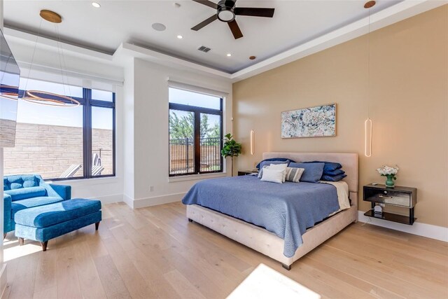 bedroom with a tray ceiling, visible vents, light wood finished floors, and baseboards