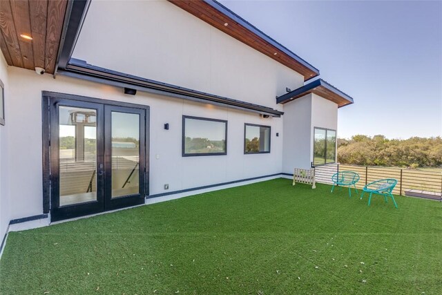rear view of property featuring fence, french doors, a yard, and stucco siding