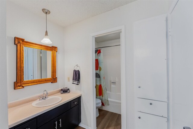 full bath with a textured ceiling, toilet, shower / tub combo, wood finished floors, and vanity