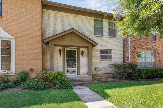 view of exterior entry with a lawn and brick siding