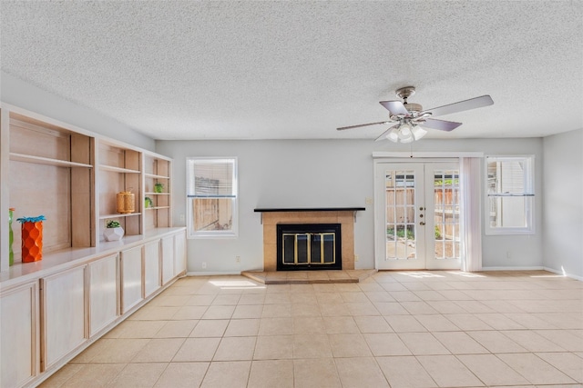 unfurnished living room featuring french doors, a textured ceiling, baseboards, a glass covered fireplace, and ceiling fan