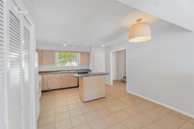 kitchen with light brown cabinets, dark countertops, a sink, light tile patterned floors, and a kitchen island