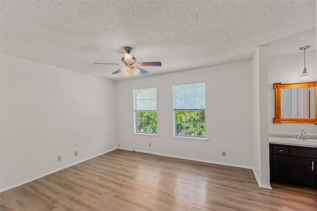 empty room with light wood-style flooring, a textured ceiling, a ceiling fan, and a sink