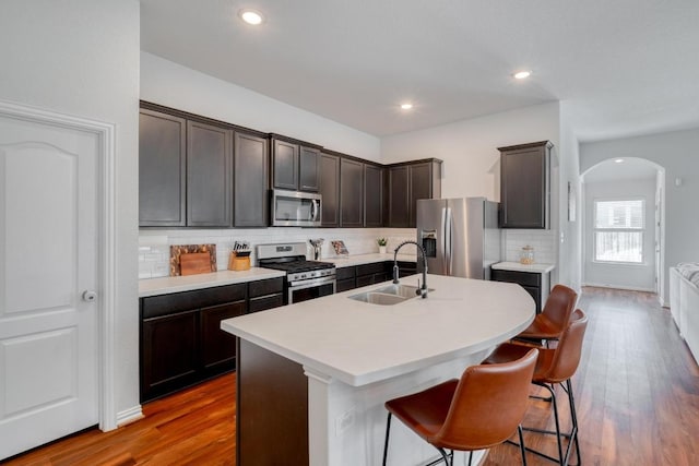 kitchen featuring tasteful backsplash, wood finished floors, a sink, arched walkways, and stainless steel appliances