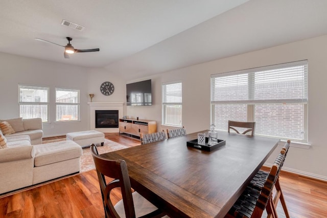 dining area featuring a healthy amount of sunlight, a glass covered fireplace, visible vents, and light wood-style flooring