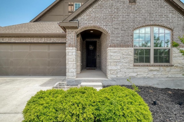 entrance to property with roof with shingles, driveway, stone siding, brick siding, and a garage