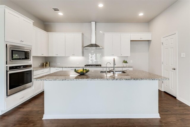 22621 Fountaingrass Ln, Lago Vista, TX 78645 - kitchen with a sink, appliances with stainless steel finishes, light stone countertops, wall chimney exhaust hood, and a kitchen island with sink