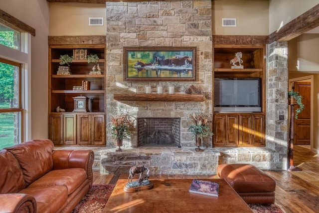 living area featuring built in shelves, wood finished floors, a stone fireplace, and visible vents