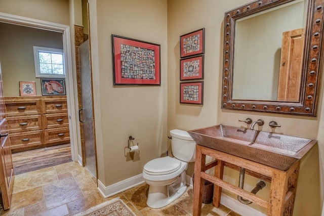 full bathroom featuring toilet, vanity, a shower, baseboards, and stone finish floor