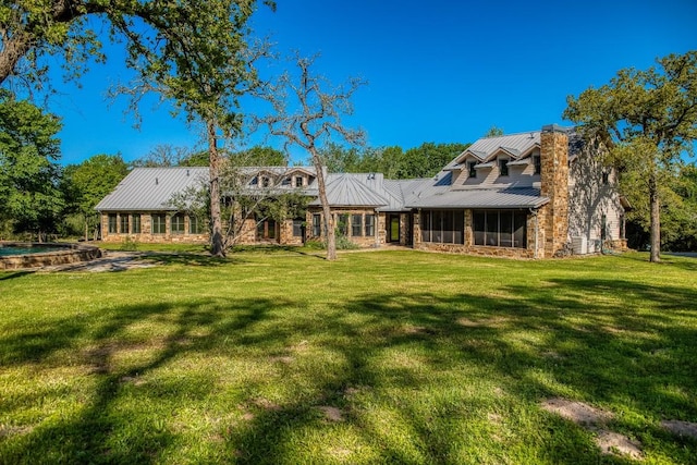 back of house with a standing seam roof, a sunroom, a yard, and metal roof