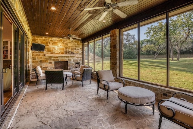 sunroom with an outdoor stone fireplace and a ceiling fan