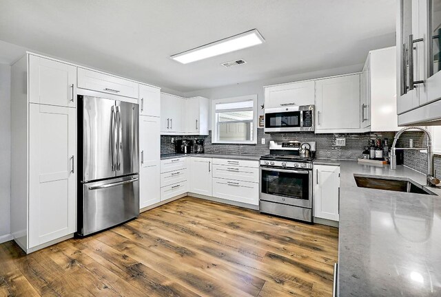 kitchen with stainless steel appliances, backsplash, visible vents, a sink, and white cabinetry