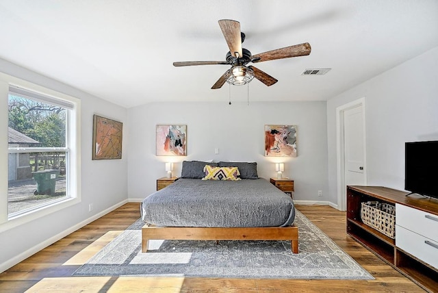 bedroom with baseboards, a ceiling fan, wood finished floors, and visible vents