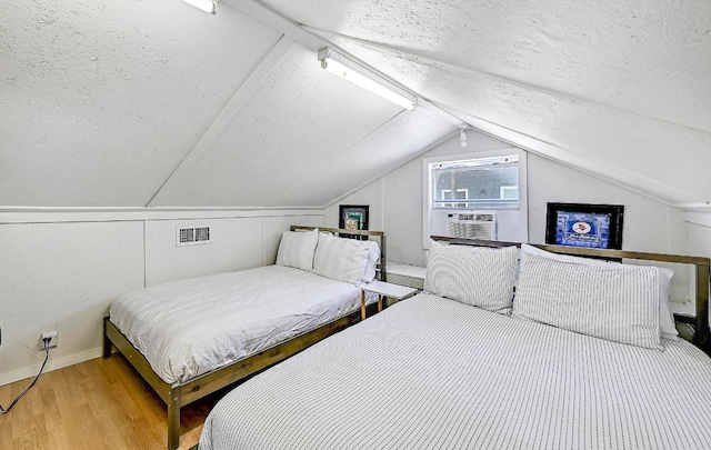 bedroom with wood finished floors, a textured ceiling, cooling unit, lofted ceiling, and visible vents
