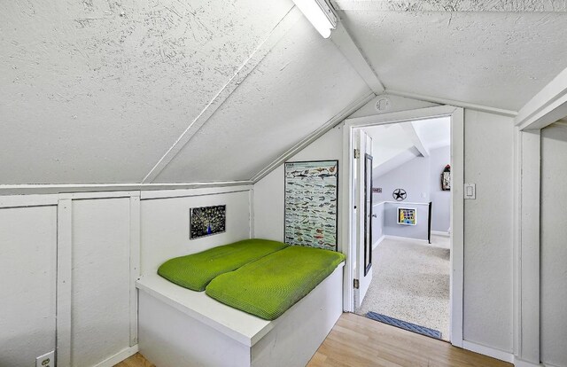 bedroom featuring vaulted ceiling, light wood-type flooring, and a textured ceiling