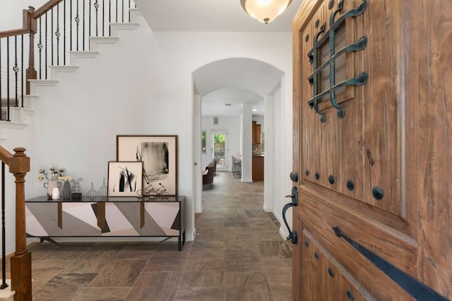 entryway featuring stone finish flooring, arched walkways, and stairs