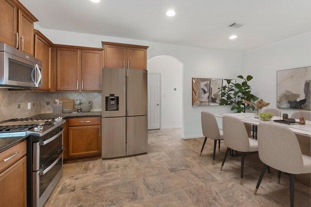 kitchen with appliances with stainless steel finishes, dark countertops, brown cabinets, and arched walkways