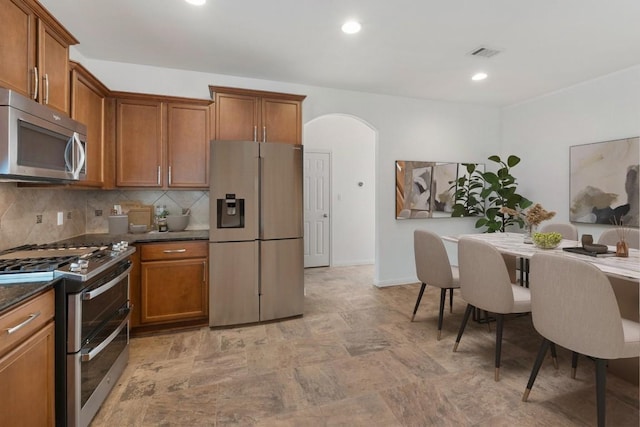 116 Silkstone St, Hutto, TX 78634 - kitchen featuring stainless steel appliances, arched walkways, dark countertops, brown cabinetry, and recessed lighting
