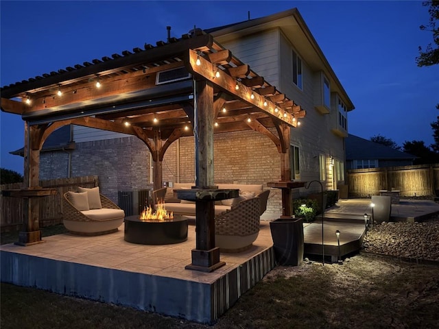 patio at twilight with a fire pit, fence, a wooden deck, cooling unit, and a pergola