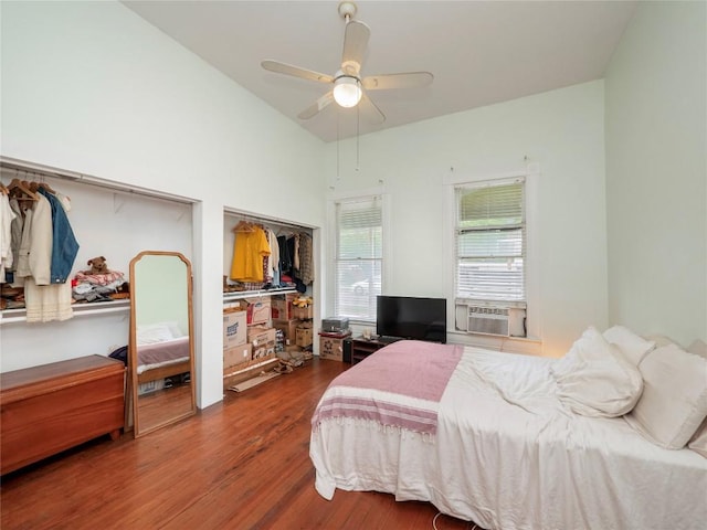 bedroom featuring vaulted ceiling, a ceiling fan, multiple closets, cooling unit, and dark wood-style flooring