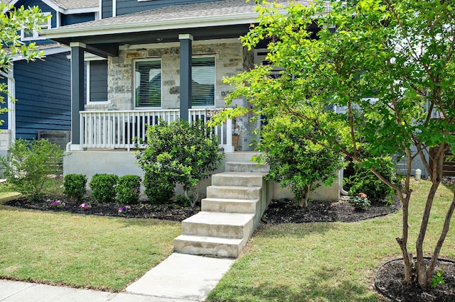 property entrance with a yard, stone siding, covered porch, and roof with shingles