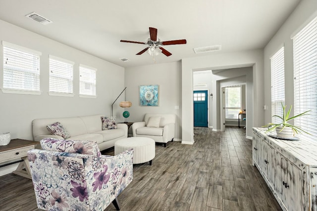 living room with dark wood-style floors, visible vents, a ceiling fan, and baseboards