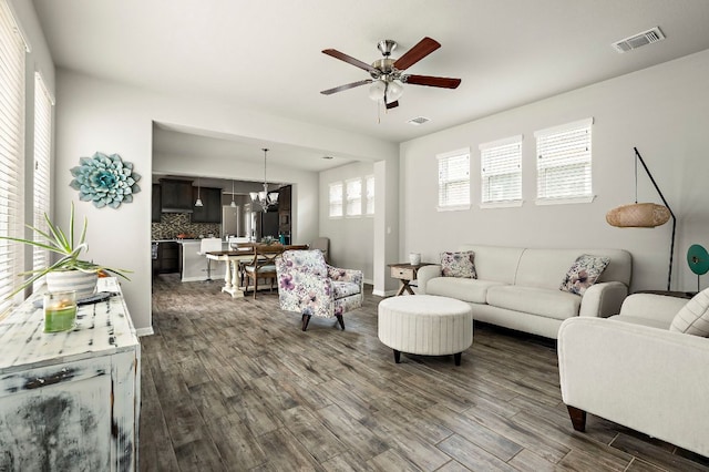 living room with dark wood-style flooring, visible vents, baseboards, and ceiling fan with notable chandelier