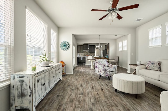 living area featuring dark wood-type flooring, visible vents, ceiling fan with notable chandelier, and baseboards