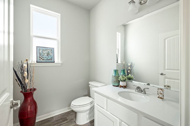 half bathroom featuring baseboards, wood finish floors, toilet, and vanity