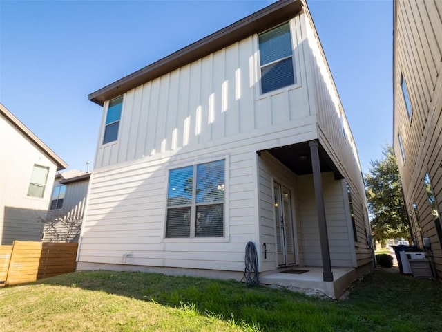 rear view of house featuring board and batten siding, fence, and a yard