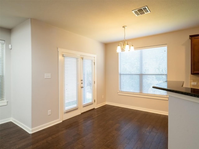 unfurnished dining area featuring baseboards, dark wood-type flooring, visible vents, and a notable chandelier