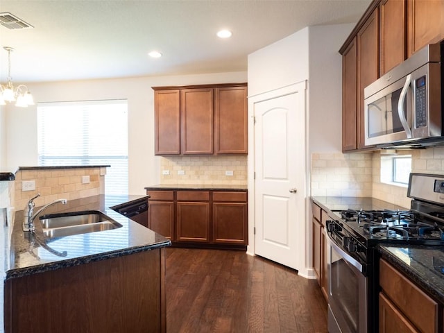 kitchen with a sink, dark stone counters, dark wood finished floors, visible vents, and appliances with stainless steel finishes
