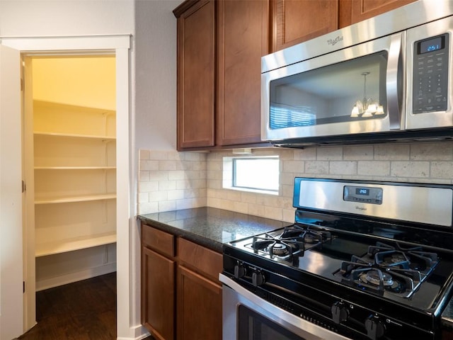kitchen featuring dark countertops, wood finished floors, brown cabinets, backsplash, and appliances with stainless steel finishes