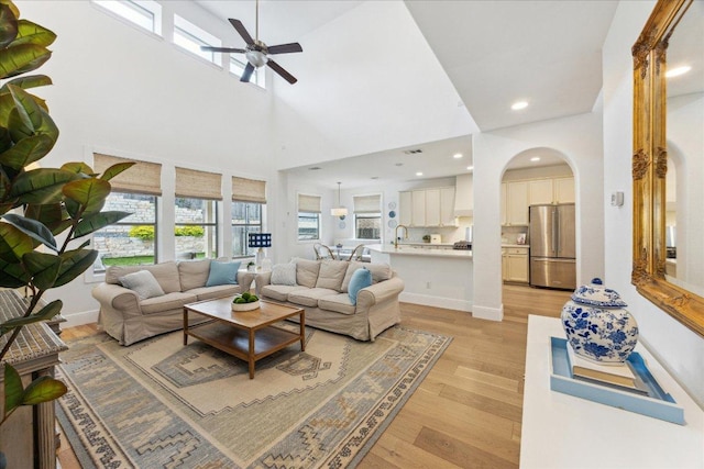 living room with ceiling fan, light wood finished floors, arched walkways, recessed lighting, and a towering ceiling