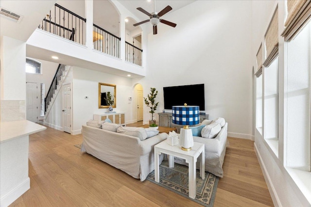 living area with arched walkways, light wood-style flooring, a high ceiling, a ceiling fan, and stairway