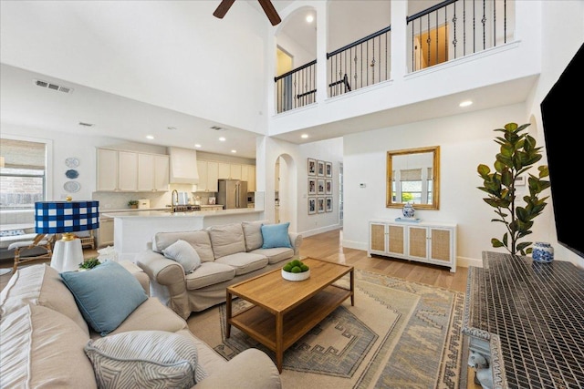 living room with light wood-style floors, ceiling fan, a towering ceiling, baseboards, and recessed lighting