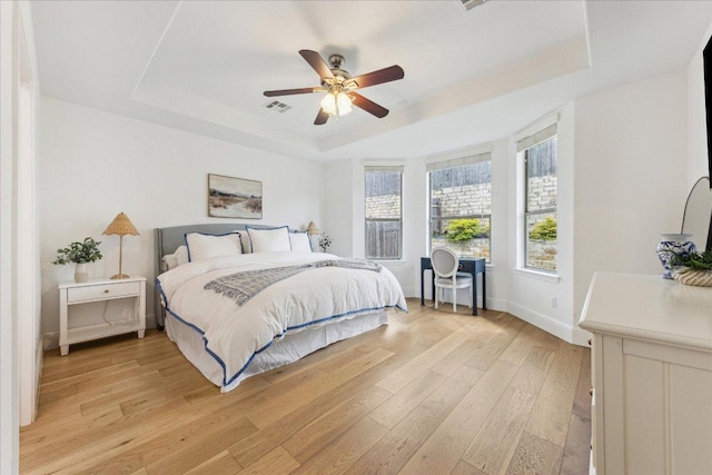 bedroom featuring a tray ceiling, light wood-style floors, multiple windows, and baseboards