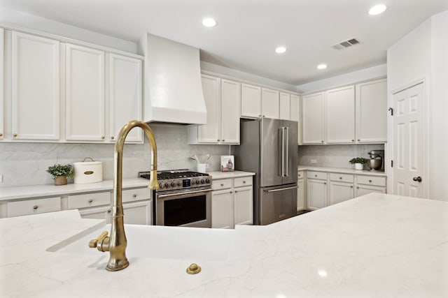 kitchen featuring stainless steel appliances, custom exhaust hood, decorative backsplash, recessed lighting, and light stone counters