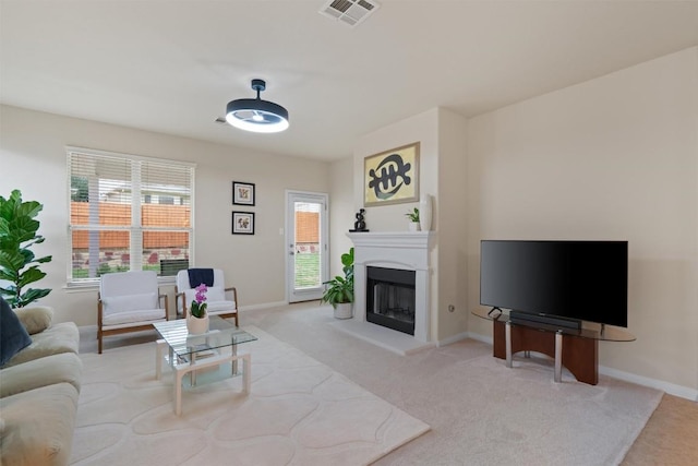 living room featuring a fireplace with raised hearth, visible vents, baseboards, and light colored carpet