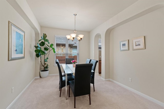 dining space with light carpet, arched walkways, baseboards, and an inviting chandelier