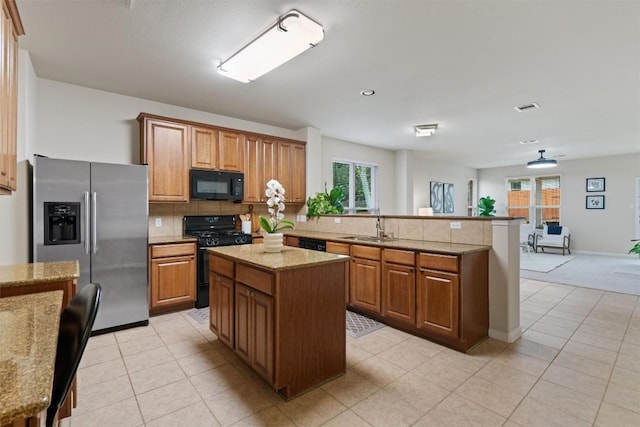 kitchen featuring visible vents, a sink, decorative backsplash, black appliances, and a peninsula