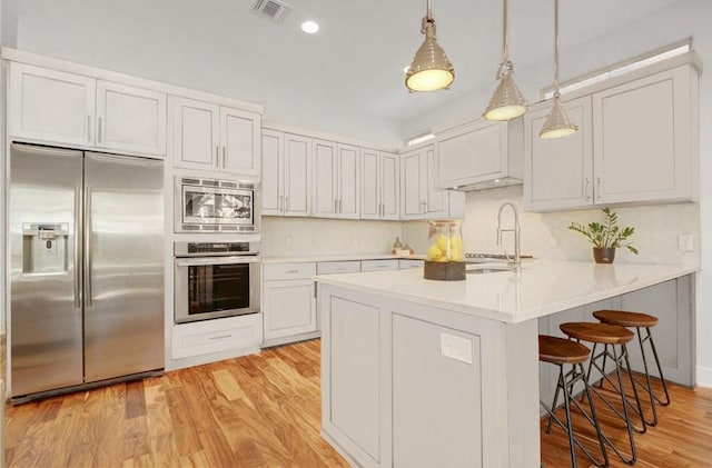 kitchen featuring visible vents, built in appliances, a peninsula, a breakfast bar area, and a sink