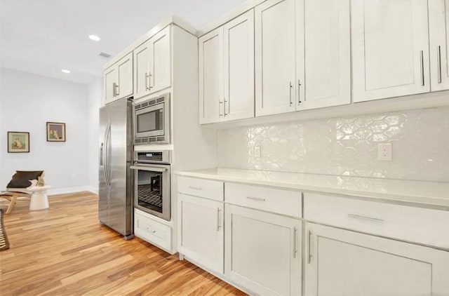 kitchen with decorative backsplash, appliances with stainless steel finishes, light wood-type flooring, light countertops, and recessed lighting