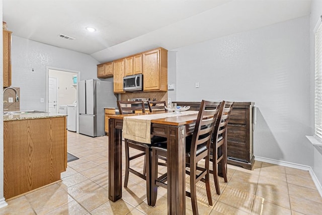 dining room with independent washer and dryer, vaulted ceiling, visible vents, and light tile patterned floors
