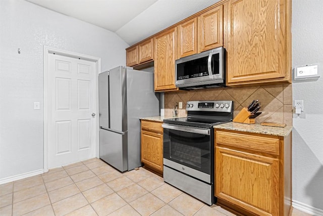 kitchen with lofted ceiling, appliances with stainless steel finishes, tasteful backsplash, and light stone countertops